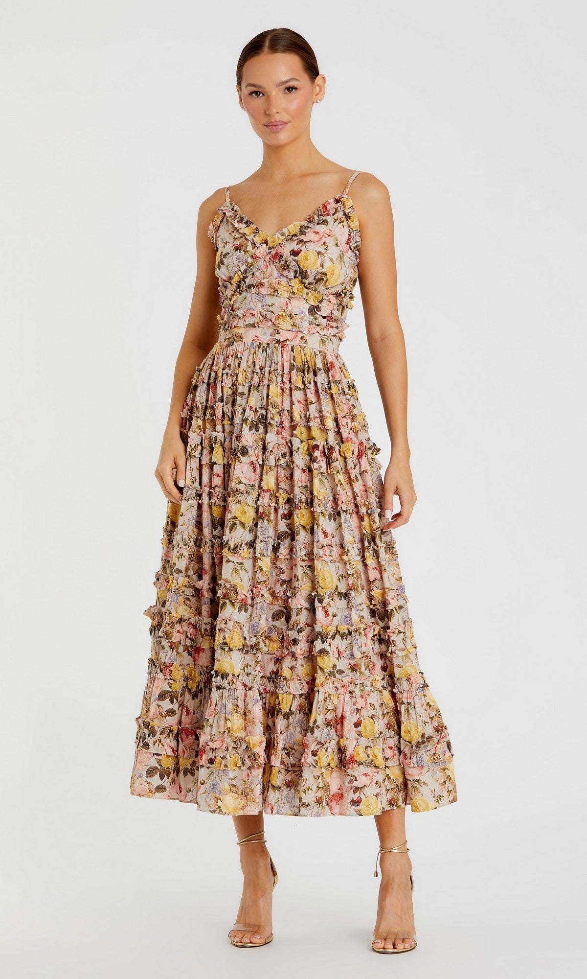 A woman wearing the Mac Duggal 8026 Midi Wedding Guest Dress in Ivory Multi, featuring thin straps and floral ruffles, paired with nude high-heeled sandals, stands against a plain white background.